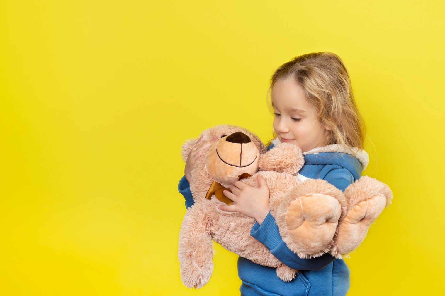 Little beautiful blonde girl hugs big teddy bear